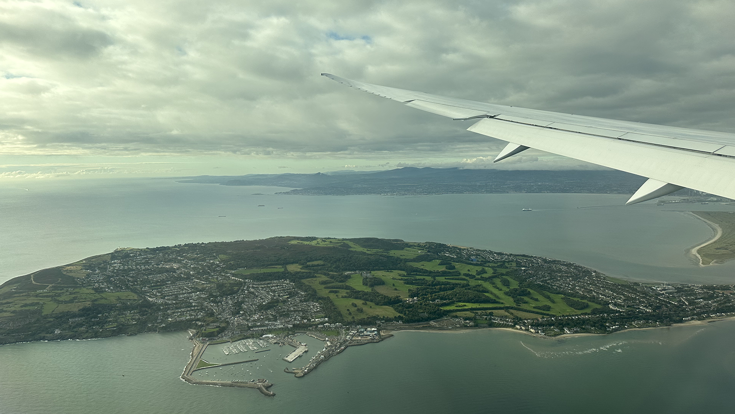 View of Howth, Ireland surrounded by the sea. Photo is taken from an airplane with the wing of the airplane visible on the top right corner of the photo.