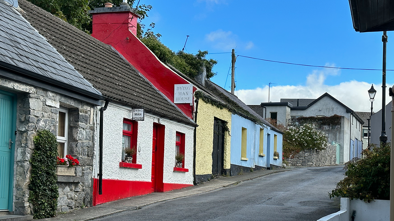 Photo of a street in a small Irish town. The street is lined with small homes, each painted a different color.